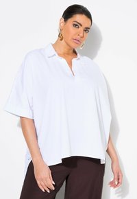 Camicia bianca over-size con colletto, maniche corte e spacchi ai lati. Presenta una superficie liscia e dettagli con bottoni lungo le maniche.
