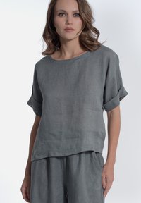 Grijze linnen top met korte mouwen, een losse pasvorm, ronde halslijn en omgeplooide mouwdetails. Gecombineerd met bijpassende lichtgrijze broek.