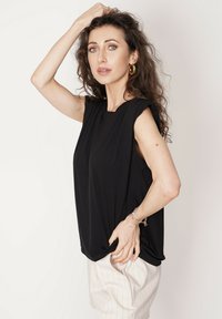 Czarny bezrękawnik o luźnym kroju, z lekko wyprofilowanymi ramionami i gładkiego materiału. W komplecie z kremowymi spodniami w paski.