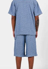 Conjunto de camisa y pantalones cortos de color azul claro con un patrón, hecho de material tejido, que presenta diseños abstractos de corazones, con mangas cortas y un corte holgado.