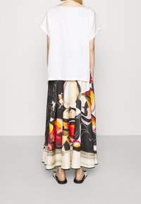 Biała krótka koszulka zestawiona z długa spódnicą sięgającą do podłogi, z wielokolorowym abstrakcyjnym wzorem na jasnym tle. Czarne sandały.