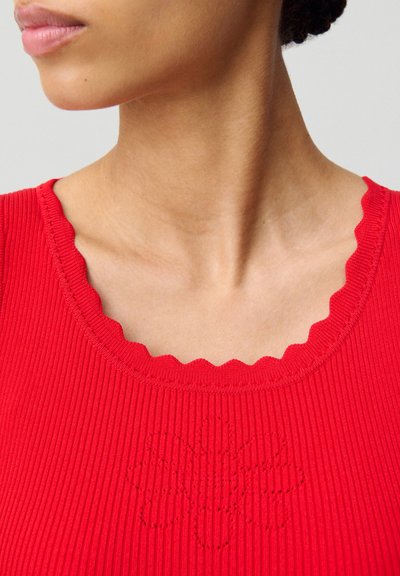 Top in maglia rossa con righe, colletto a scallop e dettagli in ricamo floreale. Il tessuto ha una consistenza liscia, che esalta il design complessivo.