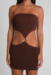 Robe mini sans bretelles en brown côtelé avec des découpes sur les côtés, présentant un accent en métal doré à la taille. Texture douce, design ajusté.