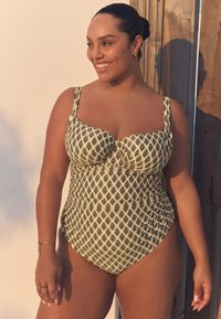 Costume intero verde e panna con motivo a rombi. Presenta coppe sagomate, spalline larghe e lati arricciati per una finitura strutturata.