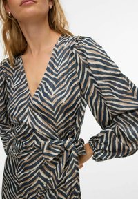 Apvīta kleita zebras rakstā ar bēša un tumši zila toņu kombināciju, pūrstām piedurknēm un jostasvietas sasiešanas detaļu.