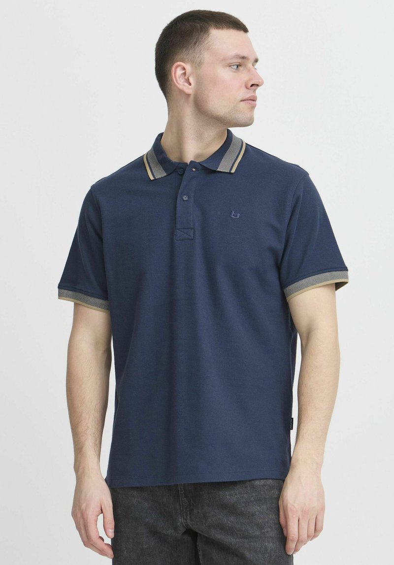 Marinblå polo skjorta med en texturerad yta, med en tvåknappsknäppning och kontrasterande krage och ärmslut i beige ränder.