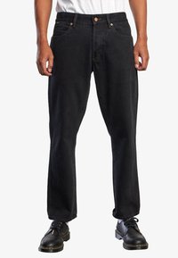 Jeans de mezclilla negra con corte recto, que cuentan con cinco bolsillos, herrajes de cobre y costuras en contraste. Combinados con zapatos negros de cordones.