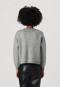 Maglione grigio a maglia con maniche lunghe e orlo a costine. Tessuto morbido, vestibilità comoda e scollatura arrotondata. Abbinato a pantaloni neri.
