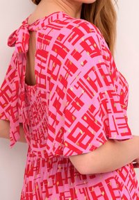 Rotes Kleid mit pinken geometrischen Mustern und goldenen Akzenten, mit einer Rückenbindung, gerafftem Oberteil, flatternden Ärmeln und lockerer Passform.