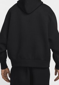 Černá oversized mikina s kapucí, měkkým materiálem, prostornou kapucí a žebrovanými manžetami a lemem, s jednoduchým a čistým designem.