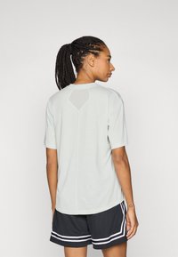 Chemise grise claire à manches courtes avec une finition texturée et une découpe en forme de losange dans le haut du dos, associée à un short noir avec des rayures blanches.