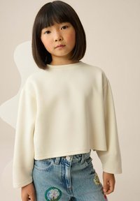 Cream-colored cropped sweatshirt with long sleeves, made from soft fabric. Worn over blue denim shorts with embroidered flower accents.