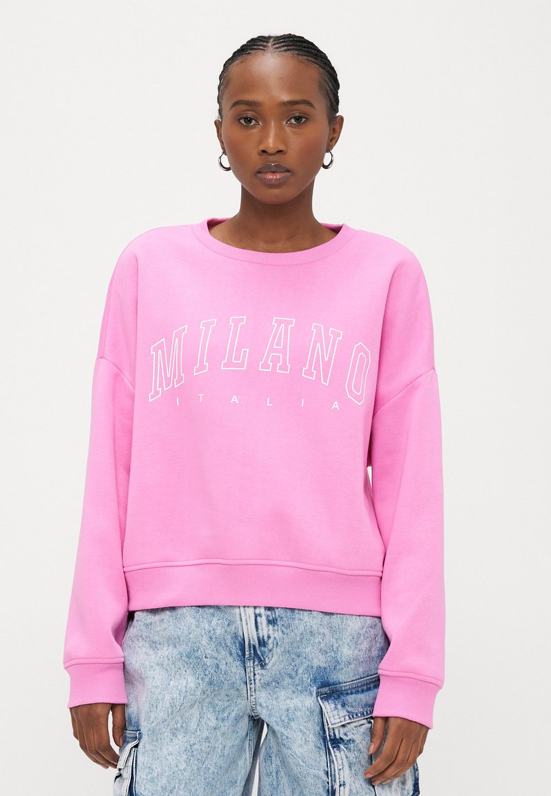 Rosa Sweatshirt mit den weißen Aufdrucken "MILANO" und "ITALIA". Hergestellt aus weichem Stoff, mit Rundhalsausschnitt und lockerem Schnitt. Kombiniert mit hellblauen Cargohosen.