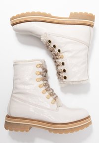 Witte gepatenteerde leren enkellaarsjes hebben een gestructureerd vetersluitingontwerp met gouden accenten en een gezellige bontvoering, gelegen op een rubberen zool.