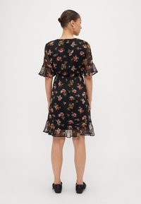 Robe noire à fleurs avec des manches courtes et volantées, une taille cintrée et un ourlet évasé, présentant des motifs floraux multicolores sur l'ensemble.