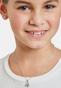 Collana d'argento con pendente floreale; piccoli orecchini a bottone con una pietra colorata. La modella indossa un top bianco a coste.