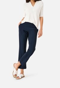 Námořnicky modré kalhoty s rovným střihem, kombinované s krémovým tričkem s krátkým rukávem a bílými sandály s křížovými pásky. Hladká textura, neformální design.