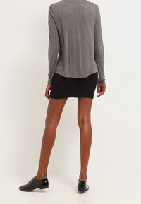 Grå långärmad tröja, lös passform, kombinerad med en svart minikjol. Svarta snörskor fulländar outfiten. Enkel och funktionell design.