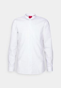 Bílá košile s dlouhým rukávem, mandlový límec, krytá léga na knoflíky a červená vnitřní štítek límce.