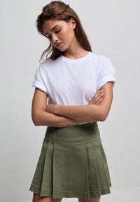 T-shirt bianco a maniche arrotolate abbinato a una gonna plissettata verde. La gonna presenta una texture liscia e una vita aderente.