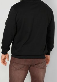 Černá mikina s dlouhými rukávy, kulatým výstřihem a žebrovanými manžetami, spojená s hnědými slim fit džíny s zadními kapsami a švy.