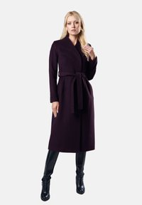 Długi płaszcz w ciemnofioletowym kolorze, wykonany z materiału o gładkiej teksturze, z długimi rękawami i paskiem do przewiązania w talii. Połączony z błyszczącymi, czarnymi trzewikami do kolan.