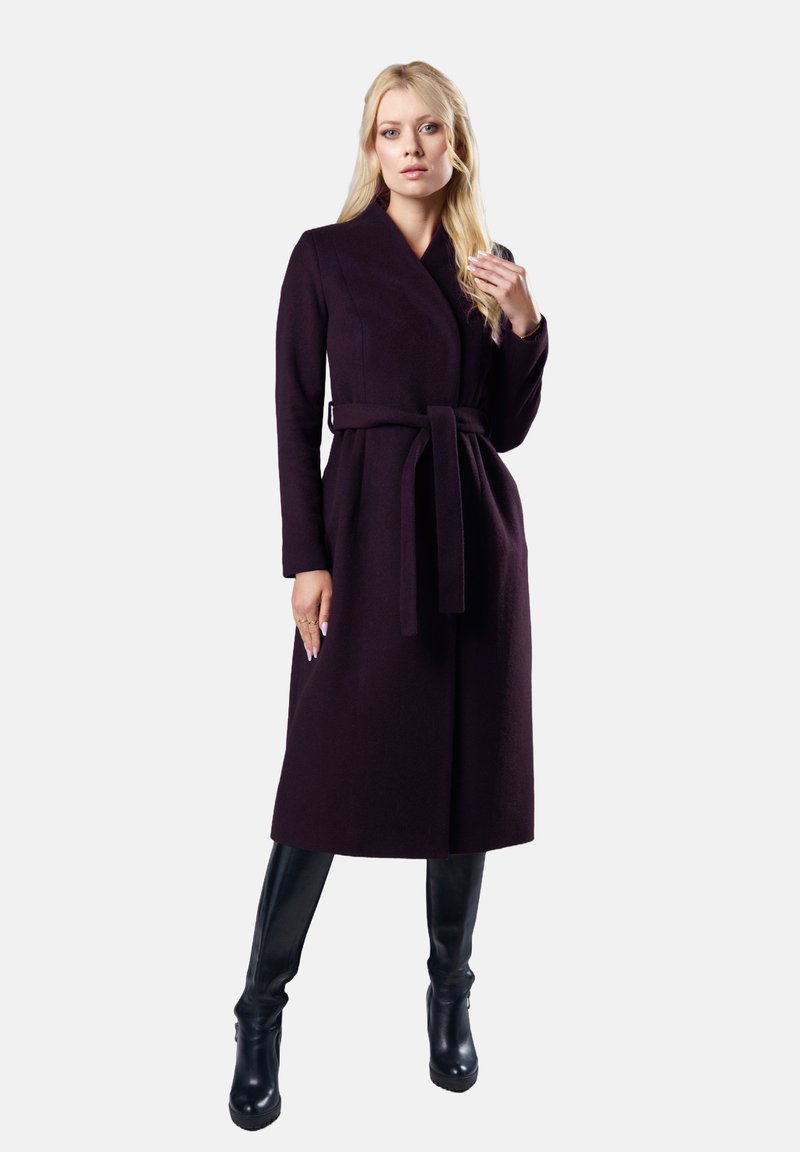 Długi płaszcz w ciemnofioletowym kolorze, wykonany z materiału o gładkiej teksturze, z długimi rękawami i paskiem do przewiązania w talii. Połączony z błyszczącymi, czarnymi trzewikami do kolan.