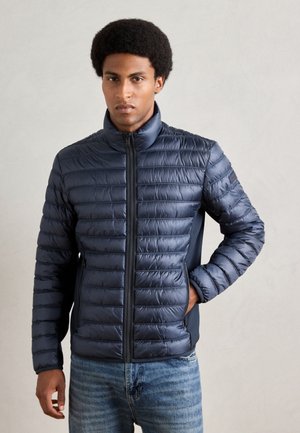 Navy puffer jacket with horizontal stitching, high collar, front zipper, and side pockets. Smooth, shiny texture, paired with blue jeans.