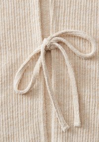 Gros plan sur un tissu tricoté de couleur crème avec un nœud attaché fait à partir d’un cordon tricoté assorti.