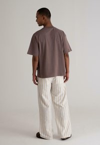 Brown oversized T-shirt with short sleeves and a crew neck, paired with white striped wide-leg pants and brown slide sandals.