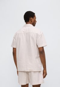 Σετ με πουκάμισο κοντομάνικο και σορτς σε ανοιχτό μπεζ με διακριτικές κάθετες ρίγες, κατασκευασμένο από μαλακό ύφασμα, με κλασικό γιακά και άνετη εφαρμογή.