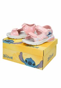 Ροζ παιδικά σανδάλια με χαρακτήρα Stitch και λουλουδάτο σχέδιο στα πλαϊνά, εκτεθειμένα πάνω σε κίτρινο κουτί παπουτσιών με το λογότυπο Disney Stitch.