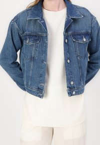 Kurtka dżinsowa w średnim odcieniu niebieskiego, z kołnierzem, zapięciem na guziki i dwoma kieszeniami na piersiach. Faktura gładka, z delikatnie wyblakłym wyglądem.