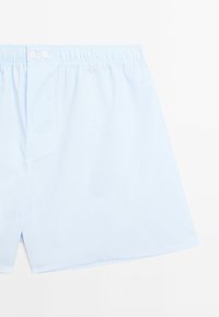 Boxers à carreaux bleu clair avec une ceinture élastique confortable et deux boutons blancs à l'avant. Texture douce et tissu respirant.