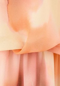 Des couches de tissu douces et fluides dans des dégradés de pêche, corail et rose clair avec de légers plis et une texture délicate.