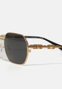 Sonnenbrille mit goldfarbenem Metallrahmen und schwarzen Gläsern. Ausgestattet mit einem Kettendesign an den Bügeln. Klare Akzente und quadratische Form.