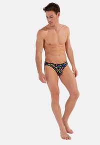 Herren-Schwimmbriefs, schwarz mit buntem Schmetterlingsmuster, tief sitzendes Design, glatte Textur und hoch geschnittene Beine für minimale Bedeckung.