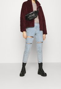Veste en polaire bordeaux, haut gris, jeans bleu clair déchirés et bottines à plateforme noires à lacets. Sac bandoulière noir avec fermetures éclair.