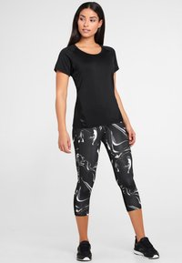 T-shirt atletico nero a maniche corte, abbinato a leggings capri con motivo marmorizzato bianco e nero. Indossato con sneakers nere.