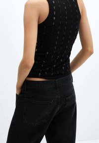 Schwarzes, geripptes Tanktop mit strukturiertem Design und dünnen Trägern, kombiniert mit hochgeschnittenen schwarzen Jeans mit Gesäßtaschen.