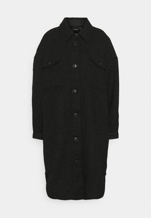 Long manteau noir boutonné avec col et deux poches poitrine à rabat, présenté sur fond blanc uni.