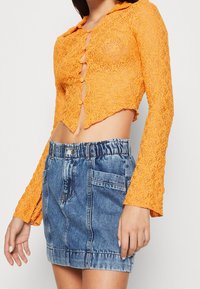 Orange spets croptop med krage och knapplist, matchat med en högmidjad denimminisärk med två framfickor.