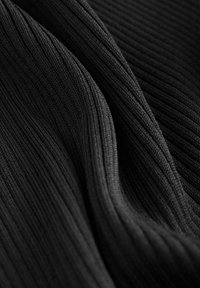 Țesătură neagră cu nervuri, cu pliuri care evidențiază textura detaliată a tricotului și liniile verticale sub o iluminare blândă.