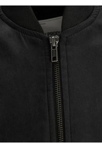 Chaqueta bomber negra con cremallera negra y cuello acanalado. La tela tiene una textura suave con un acabado mate.