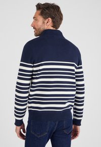 Pull rayé bleu marine et blanc avec un col haut, fabriqué dans un tissu doux. Features des poignets et un ourlet côtelés, avec une petite étiquette logo sur le côté.