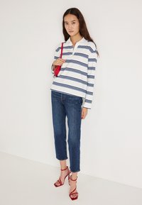 Λευκό πουκάμισο με μακριά μανίκια και ναυτικές ρίγες, συνδυασμένο με σκουρομπλε κοντά τζιν και κόκκινες πέδιλα με λουράκια. Απλός σχεδιασμός, καθημερινή εφαρμογή.