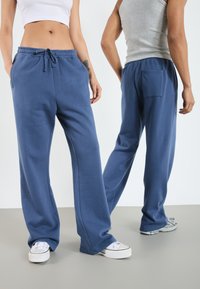 Blå bomullsmjukisbyxor med avslappnad passform, elastisk midja, dragsko, sidofickor och en bakficka, i kombination med vita sneakers.