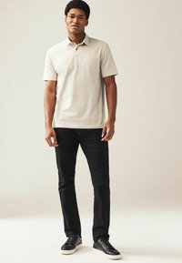 Camisa polo gris claro con cuello, combinada con jeans ajustados negros y zapatillas negras. Diseño minimalista con un sutil detalle del logo.