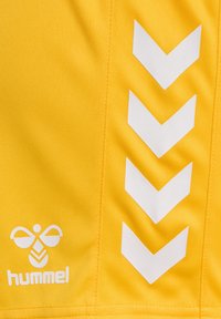 Gul tyg med en slät textur, prydd med vita chevron-ränder och en vit logotyp i nedre vänstra hörnet.