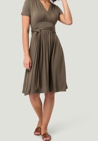 Robe portefeuille vert olive à manches courtes, taille froncée et jupe longueur genou. Fabriquée dans un tissu doux et extensible, avec un détail de nœud sur le côté.
